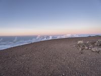 a lone man standing at the top of a hill and looking at the clouds below him