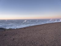 a lone man standing at the top of a hill and looking at the clouds below him