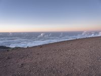 a lone man standing at the top of a hill and looking at the clouds below him