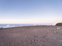 a lone man standing at the top of a hill and looking at the clouds below him