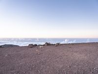 a lone man standing at the top of a hill and looking at the clouds below him