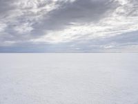 a man walking across a large open field covered in snow and clouds that is cloudy