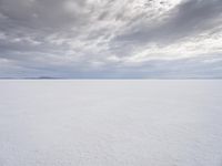 a man walking across a large open field covered in snow and clouds that is cloudy