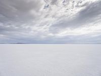 a man walking across a large open field covered in snow and clouds that is cloudy