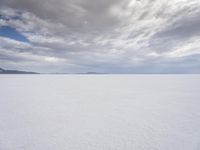 a man walking across a large open field covered in snow and clouds that is cloudy