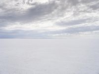 a man walking across a large open field covered in snow and clouds that is cloudy