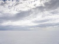 a man walking across a large open field covered in snow and clouds that is cloudy