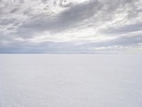 a man walking across a large open field covered in snow and clouds that is cloudy