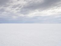 a man walking across a large open field covered in snow and clouds that is cloudy