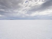 a man walking across a large open field covered in snow and clouds that is cloudy