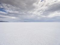 a man walking across a large open field covered in snow and clouds that is cloudy