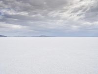 a man walking across a large open field covered in snow and clouds that is cloudy