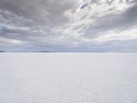 a man walking across a large open field covered in snow and clouds that is cloudy