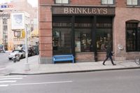 a man is walking on the sidewalk in front of a bricked building with an advertisement for brinkly's