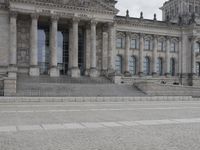 man walking with a backpack on the cobblestone street next to a building with columns