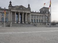 man walking with a backpack on the cobblestone street next to a building with columns