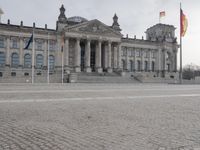 man walking with a backpack on the cobblestone street next to a building with columns