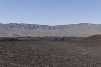 a man walking on a field in a desert land with a motorcycle behind him and a mountain in the distance