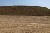 a man is walking through an empty field in front of a large mound of dirt