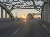 a man walking across an empty highway with the sun setting over the bridge behind him