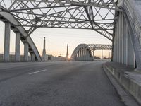 a man walking across an empty highway with the sun setting over the bridge behind him