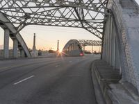 a man walking across an empty highway with the sun setting over the bridge behind him