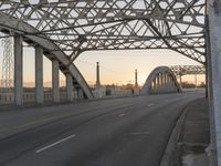 a man walking across an empty highway with the sun setting over the bridge behind him