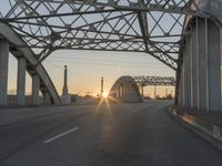 a man walking across an empty highway with the sun setting over the bridge behind him