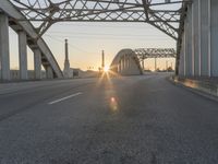 a man walking across an empty highway with the sun setting over the bridge behind him