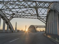 a man walking across an empty highway with the sun setting over the bridge behind him