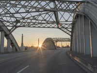 a man walking across an empty highway with the sun setting over the bridge behind him