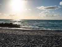 a man is walking on the beach with his surf board during a beautiful sunset with bright sunlight