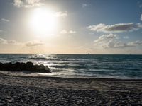 a man is walking on the beach with his surf board during a beautiful sunset with bright sunlight