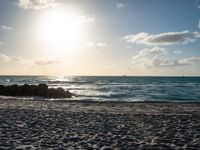 a man is walking on the beach with his surf board during a beautiful sunset with bright sunlight