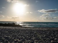 a man is walking on the beach with his surf board during a beautiful sunset with bright sunlight