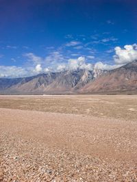 a man walking in the desert toward some mountains and clouds with mountains in the background