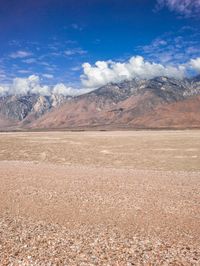 a man walking in the desert toward some mountains and clouds with mountains in the background