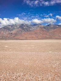 a man walking in the desert toward some mountains and clouds with mountains in the background