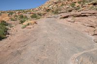 a man is walking on an old road in the desert side way next to a steep hill