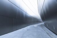 a man walking on the side of a road near a metallic wall of a building