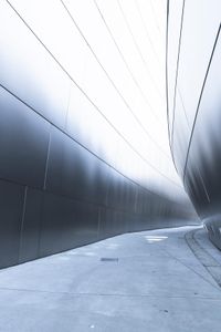 a man walking on the side of a road near a metallic wall of a building