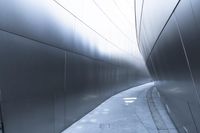 a man walking on the side of a road near a metallic wall of a building