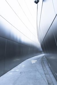 a man walking on the side of a road near a metallic wall of a building