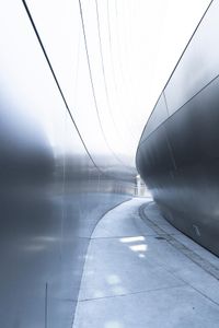 a man walking on the side of a road near a metallic wall of a building