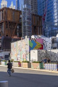 a man walking down the road in front of some tall buildings under construction with a colorful painting on them