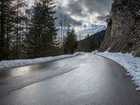 the man walks down the snowy road through the forest, near the steep side of the mountain