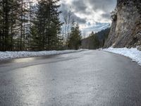 the man walks down the snowy road through the forest, near the steep side of the mountain