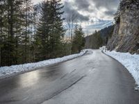 the man walks down the snowy road through the forest, near the steep side of the mountain