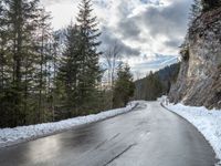 the man walks down the snowy road through the forest, near the steep side of the mountain