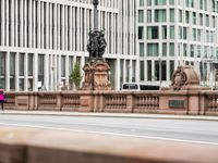 a man walks across the street in front of a stone lion statue and some building